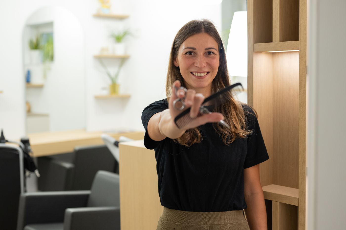 Gisi lächelt und hält Schere und Kamm in die Kamera